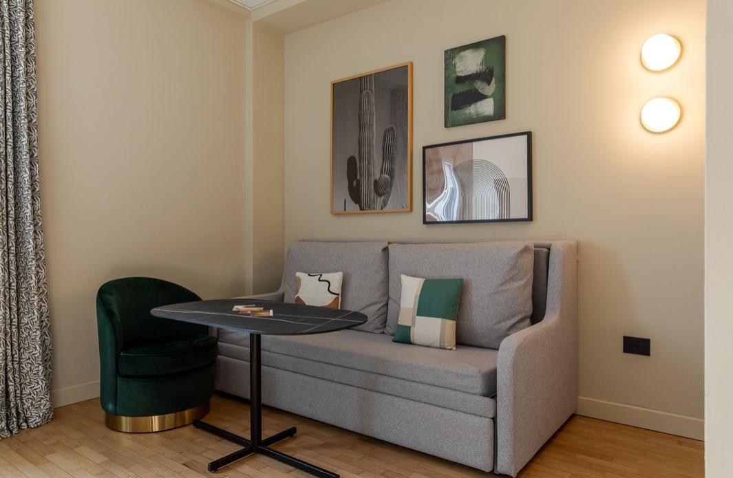 Angolo salotto moderno con divano grigio, tavolino e poltrona verde.