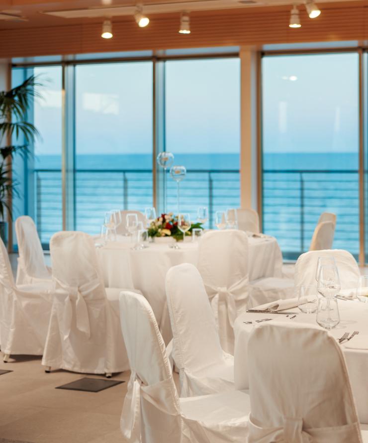 Sala elegante con vista mare, tavoli apparecchiati con fiori.