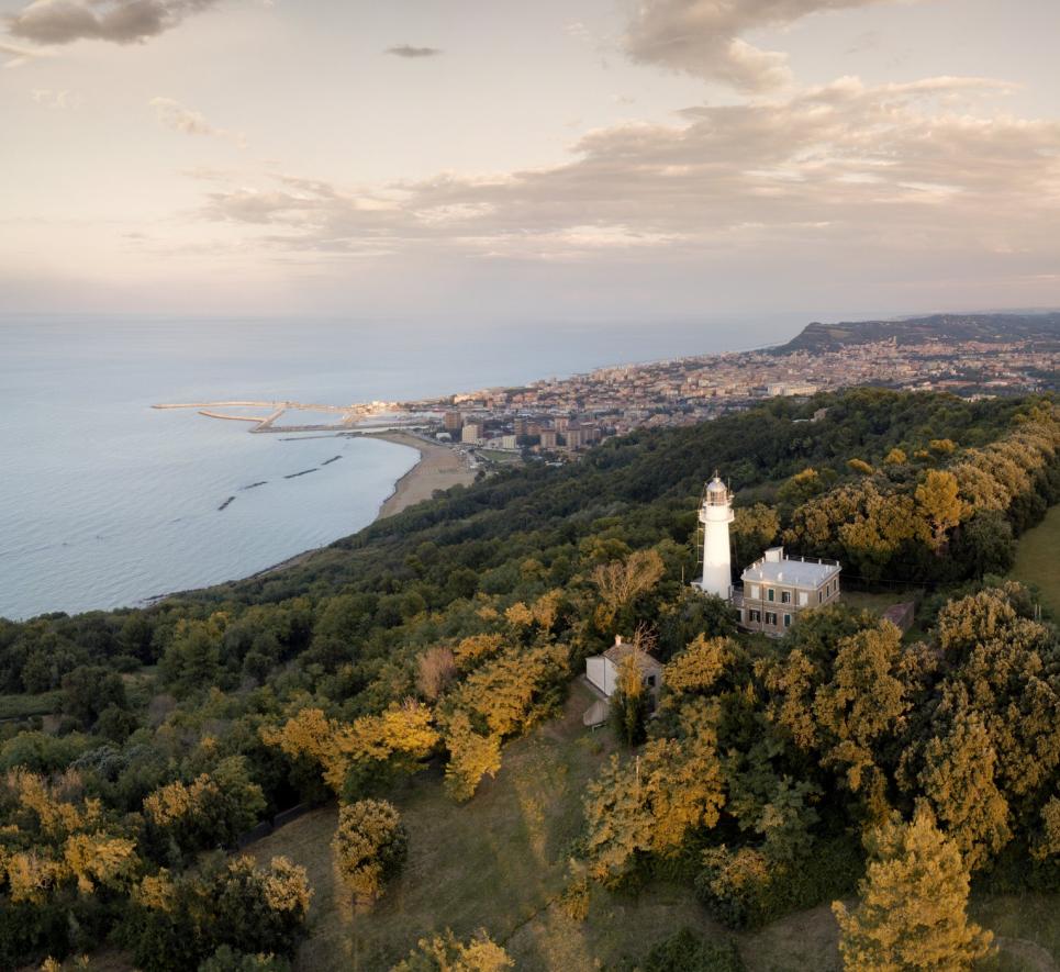 Vista costiera con faro e città sullo sfondo al tramonto.